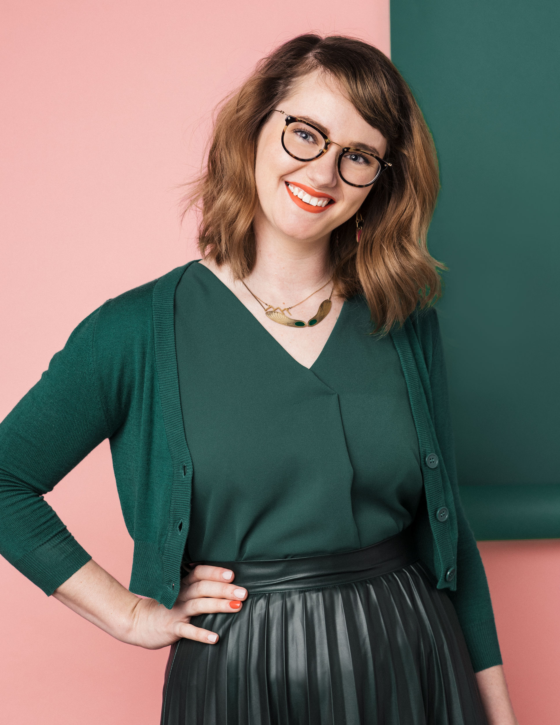Katie Moody in her glasses and a cute green monochromatic set in front of a pink and green backdrop